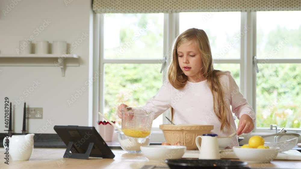 Girl wearing pyjamas baking in kitchen at home following recipe on digital tablet and pouring mixture into bowl - shot in slow motion Girl wearing pyjamas baking in kitchen at home following recipe on digital tablet and pouring mixture into bowl - shot in slow motion