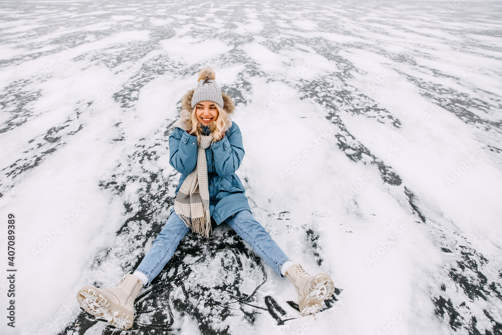 Cheerful young woman sitting on ice, smiling, on a cold winter day.