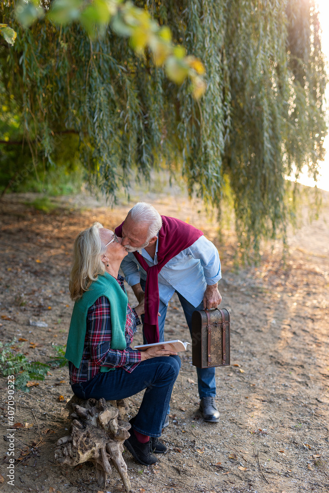 A happy elderly couple is kissing and enjoying the picnic at the riverside. A happy elderly couple is kissing and enjoying the picnic at the riverside.