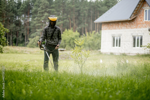 Worker with a gas mower in his hands, mowing grass in front of the house. Trimmer in the hands of a man. Gardener cutting the grass. Lifestyle.