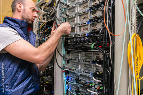 The specialist works with computer equipment in the data center. The man serves the server hardwareA technician switches internet wires in a server room.