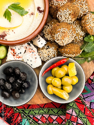 Roasted chickpeas falafel patties with a plate of Hummus, served with fresh vegetables and olives in a wooden plate over light background. Healthy vegan food, clean eating, dieting, top view