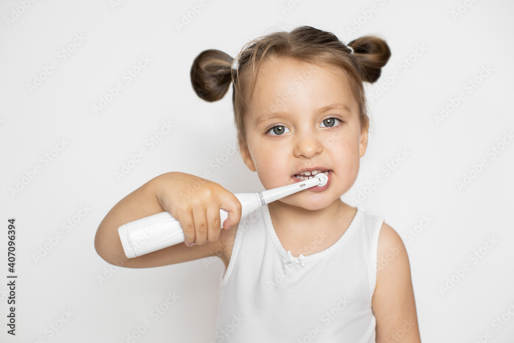 Little cute blond girl brushing her teeth with electric toothbrush. Oral teeth care and caries prevention. Close up horizontal studio shot on isolated white background Little cute blond girl brushing her teeth with electric toothbrush. Oral teeth care and caries prevention. Close up horizontal studio shot on isolated white background