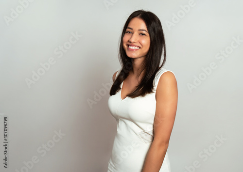Beautiful young woman with long black hair posing in dress on grey background