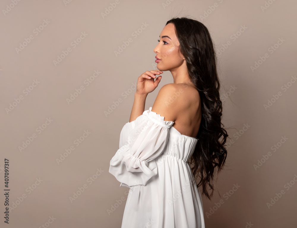 Beautiful young woman with long shiny black hair and natural make-up posing in dress on grey background Beautiful young woman with long shiny black hair and natural make-up posing in dress on grey background
