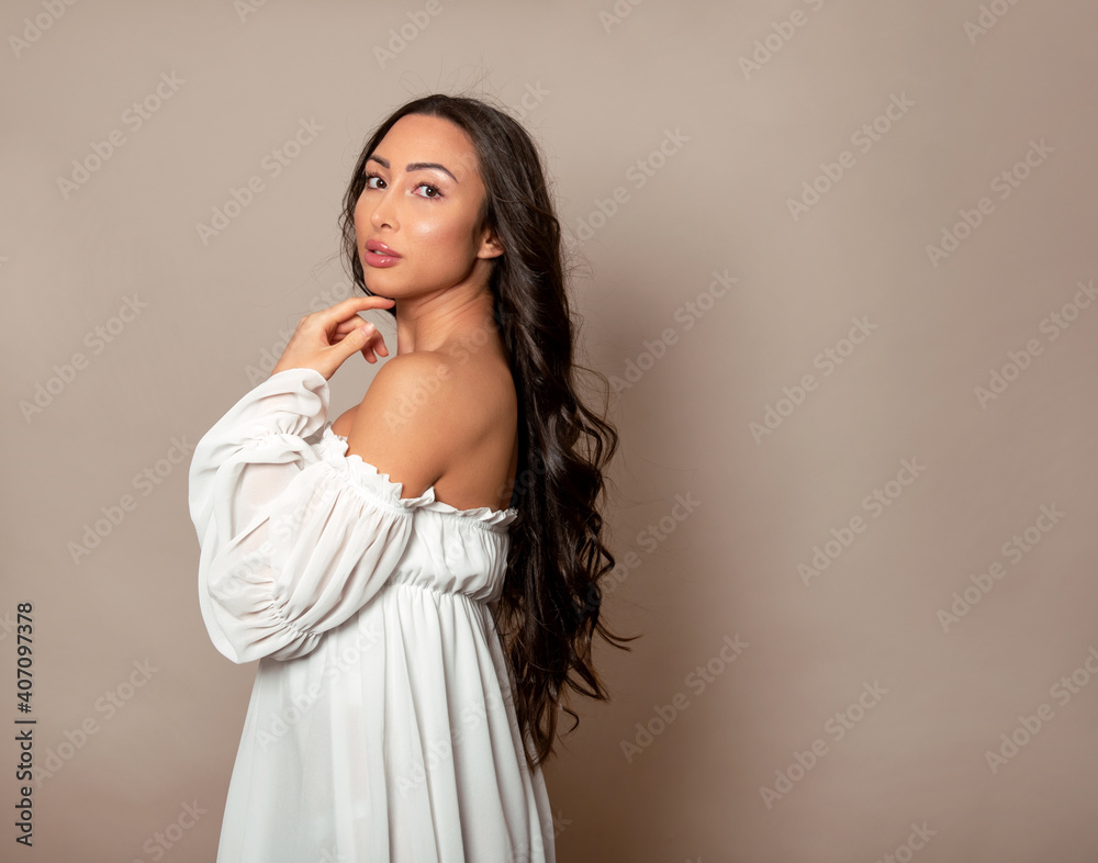 Beautiful young woman with long shiny black hair and natural make-up posing in dress on grey background Beautiful young woman with long shiny black hair and natural make-up posing in dress on grey background