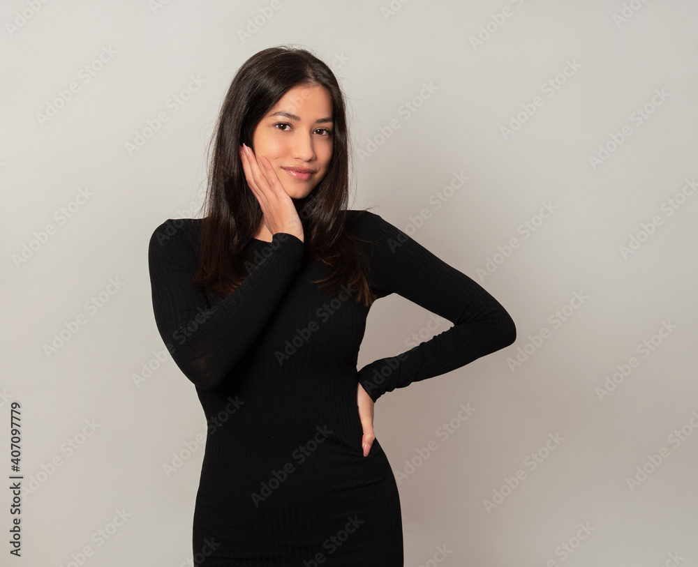 Beautiful young woman with long black hair posing in dress on grey background Beautiful young woman with long black hair posing in dress on grey background