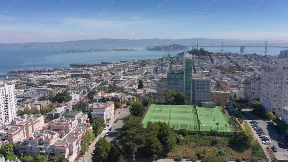 San Francisco aerial. World Famous curved Lombard street and bay view USA. People playing on green tennis and basketball courts at outdoor sport playground in George Sterling Park on sunny summer day. San Francisco aerial. World Famous curved Lombard street and bay view USA. People playing on green tennis and basketball courts at outdoor sport playground in George Sterling Park on sunny summer day.