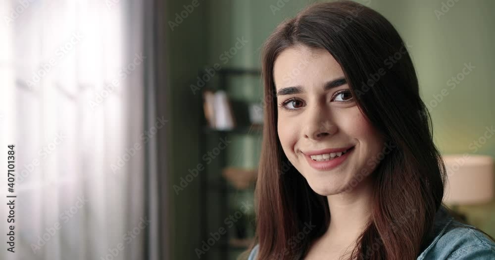 Camera approaching Caucasian young joyful happy pretty female teen with smile on face standing in living room in apartment, looking at camera and smiling, positive emotions, close up concept Camera approaching Caucasian young joyful happy pretty female teen with smile on face standing in living room in apartment, looking at camera and smiling, positive emotions, close up concept