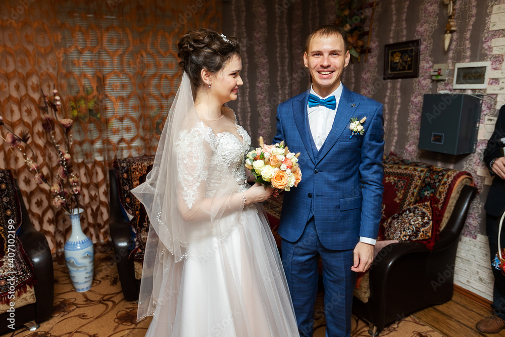 a young bride kisses and hugs the groom in the home interior, meeting the elegant lovers of the newlyweds before the wedding ceremony a young bride kisses and hugs the groom in the home interior, meeting the elegant lovers of the newlyweds before the wedding ceremony
