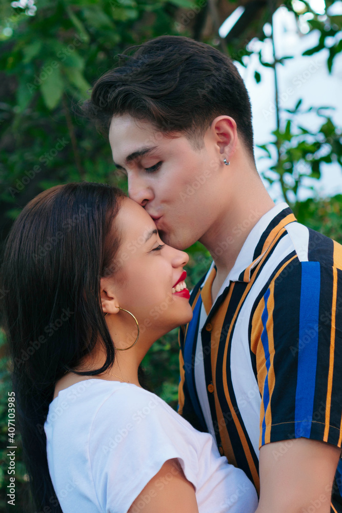 Portrait of a handsome young man kissing the forehead of his beautiful girlfriend, romantic couple relationship, side view with blurred nature background. Portrait of a handsome young man kissing the forehead of his beautiful girlfriend, romantic couple relationship, side view with blurred nature background.