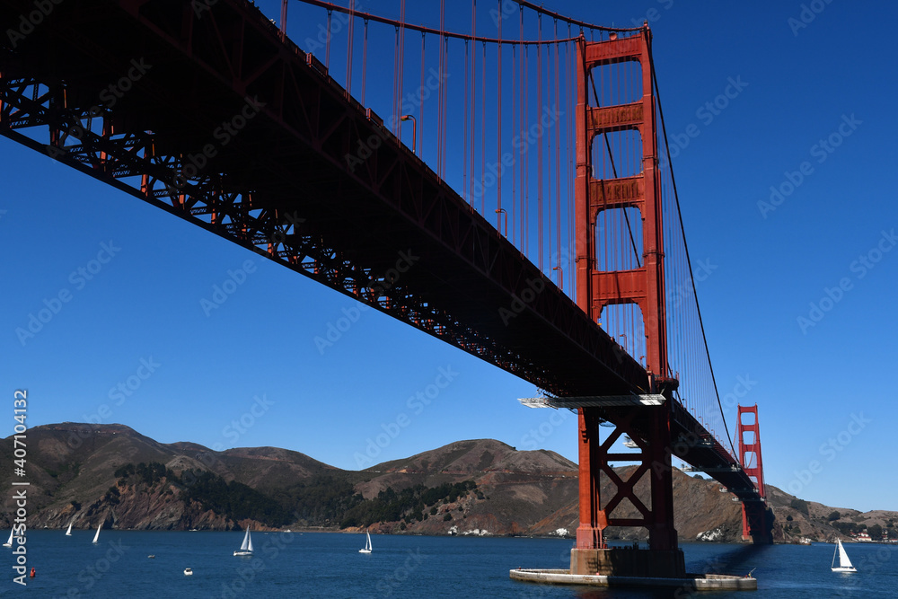 Golden Gate Bridge, seen from below, and white sailboats on the Golden Gate strait on a sunny day with a cloudless blue sky