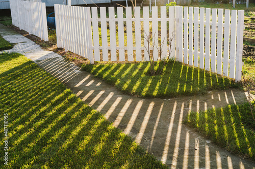 Linear shadow from a white fence is reflected on a green lawn