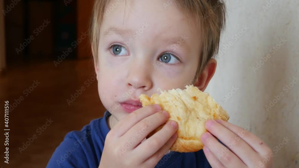 A little boy sits and eats an appetizing bun looking at the distance close-up A little boy sits and eats an appetizing bun looking at the distance close-up