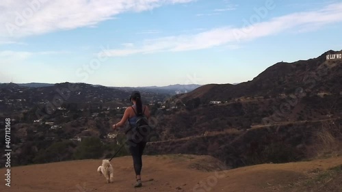 Slow motion Hispanic female walking dog down hills, passes Hollywood sign