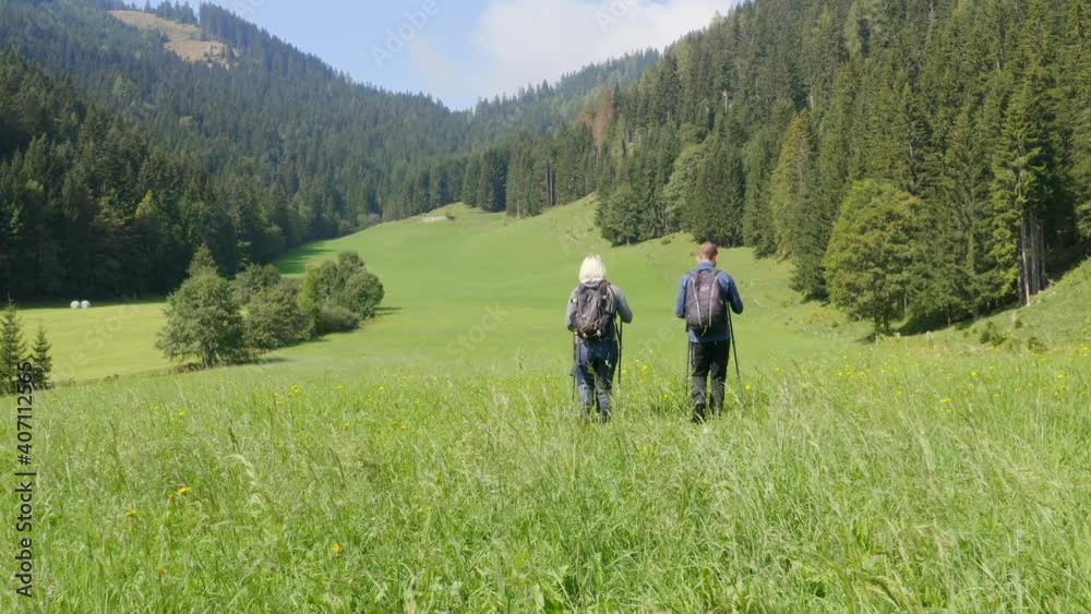 Couple with backpacks is hiking on the hill with the background of mountains and green fields. Couple with backpacks is hiking on the hill with the background of mountains and green fields.