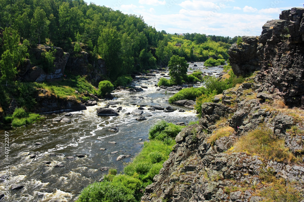 A fast mountain river flows between green banks A fast mountain river flows between green banks