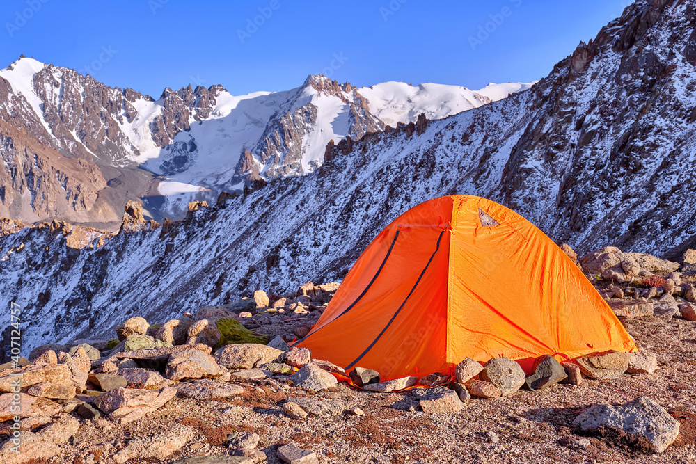 Tent is placed on a mountain ridge and reinforced with stones around the perimeter for increased wind resistance; travel and tourism concept