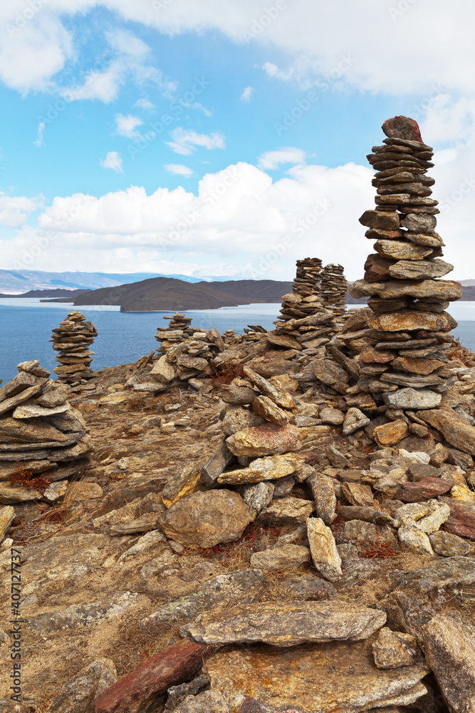 Baikal Lake in the spring. A ritual stone pile of pyramids and cairns on top of a rock against a blue sky. Ice drift in the Strait of Olkhon Gate. Spring travel. Natural background