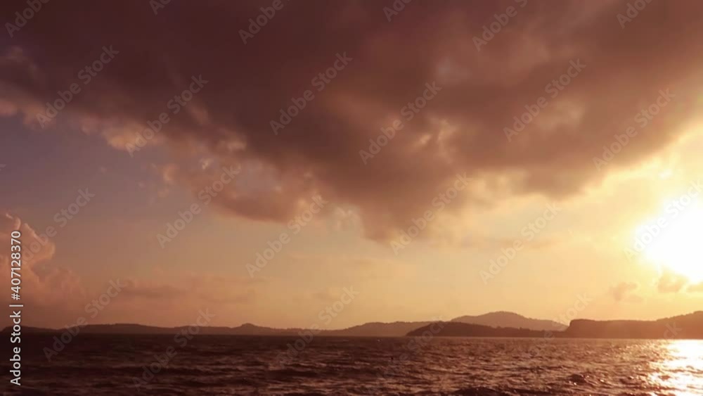 Glowing sea water surface n calm ocean wave with Colorful pastel red orange purple pink cloud n dark gray n white cloudscape in bright sun light ray n bokeh lens flare effect, 4k cinemagraphs b-roll