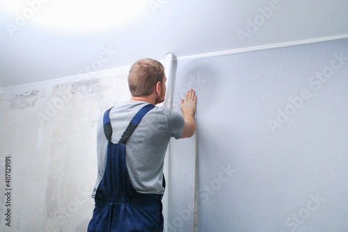 A man glues gray vinyl wallpaper on a non-woven backing. Renovation of the room.