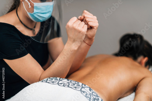 Lomilomi Practitioner wearing a Protective Mask, Giving Back Massage at a Wellness Center photo