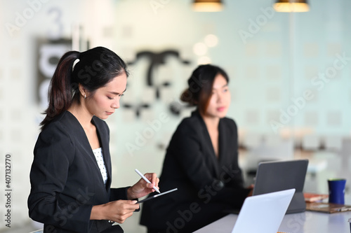 Businesswoman sitting in office with her colleague and writing business plan on notebook.
