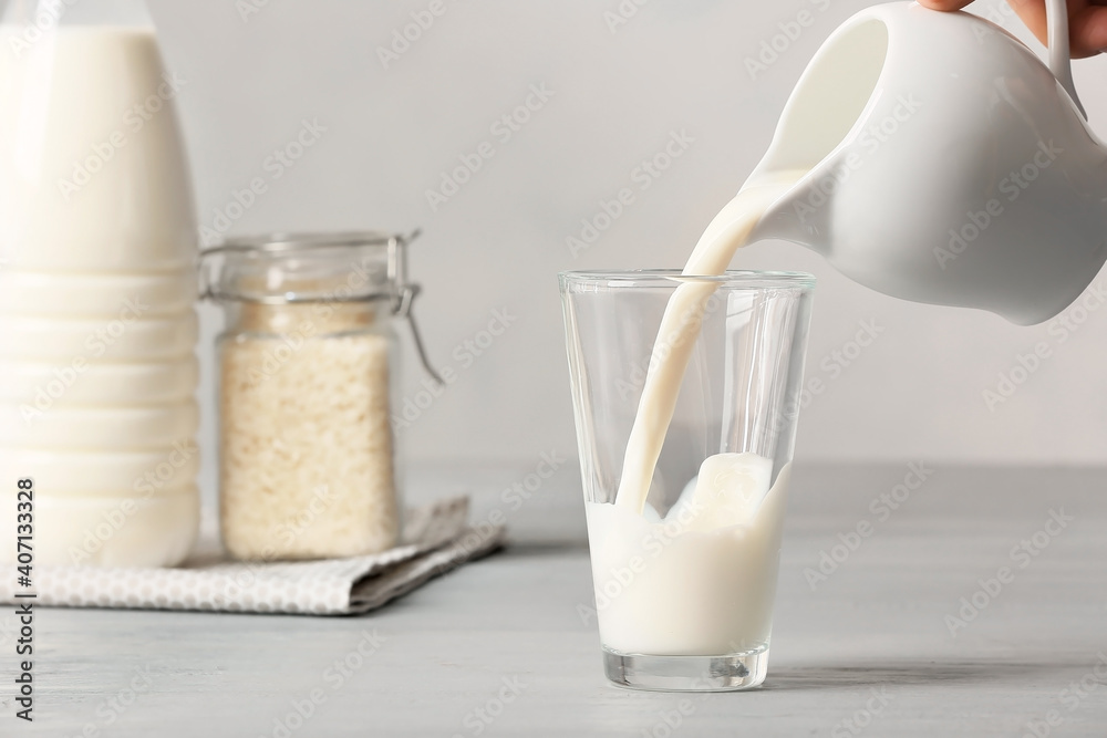 Pouring of rice milk from jug into glass on table Pouring of rice milk from jug into glass on table