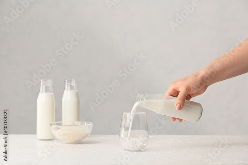 Woman pouring rice milk from bottle into glass on table