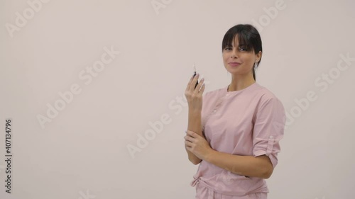 Cosmetologist in uniform shows modern tattoo machine posing for camera on beige background with space for design slow motion