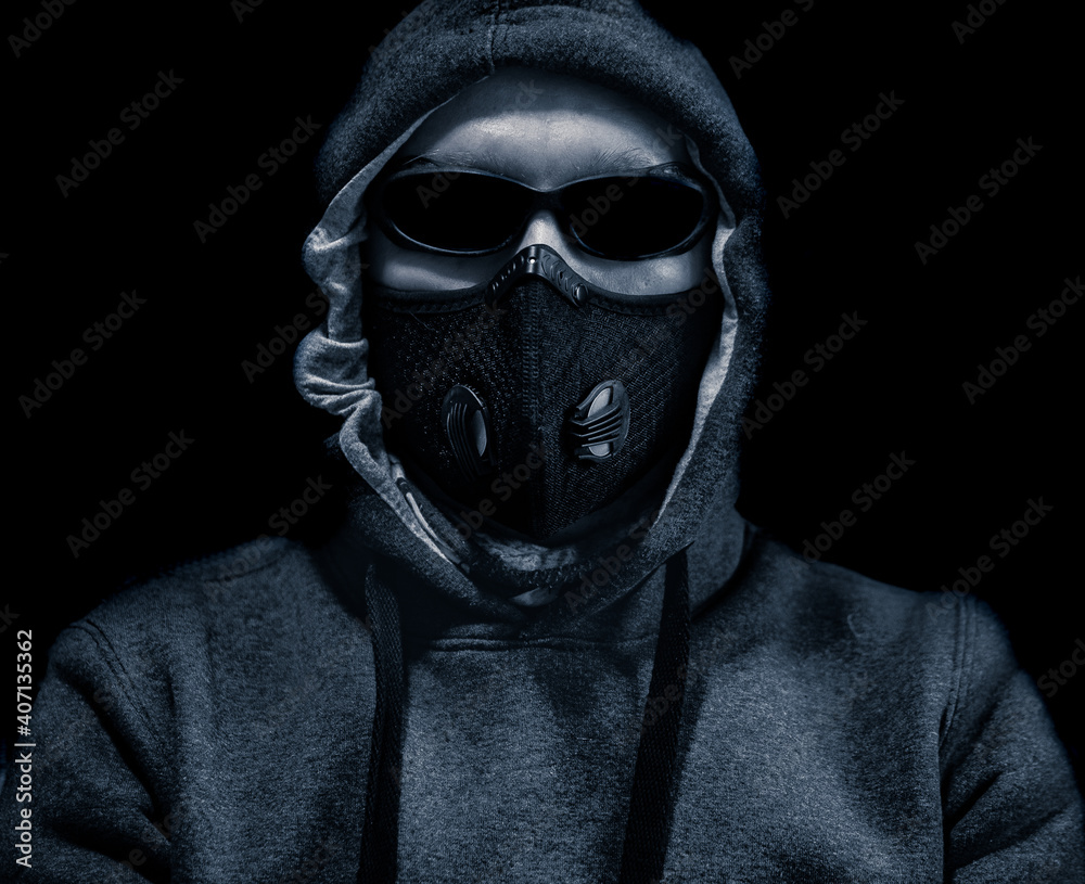 Head with black glasses a hood and a protective mask on a black background. Close Up view. Portrait of the anonymous in black with respirator on dark background.