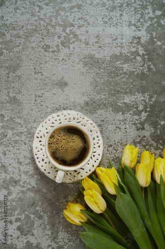 cup of black coffee on stone surface and bouquet of yellow tulips