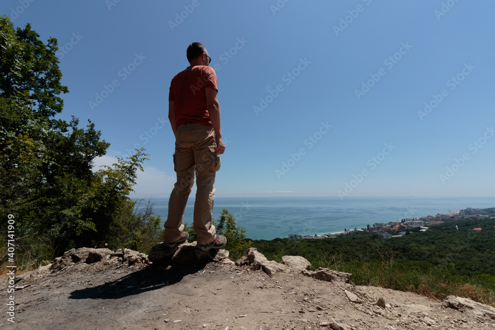 man standing and looking at the sea coast from the top of a hill
