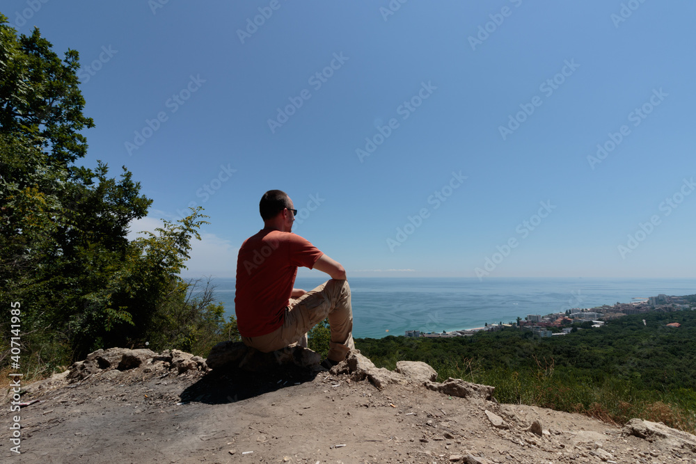 man sitting and looking at the sea coast from the top of a hill