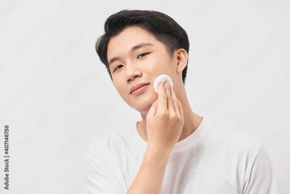 Facial care. Portrait of a positive delighted nice man holding a cotton pad and using it while caring about his face Facial care. Portrait of a positive delighted nice man holding a cotton pad and using it while caring about his face