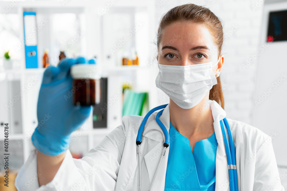 Female doctor in mask holding glass jar with medicine Female doctor in mask holding glass jar with medicine