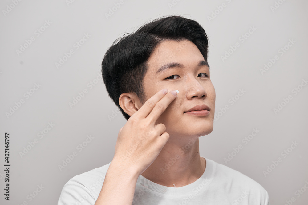 Skin care. Portrait of handsome young man applying cream to his face, isolated on white background Skin care. Portrait of handsome young man applying cream to his face, isolated on white background