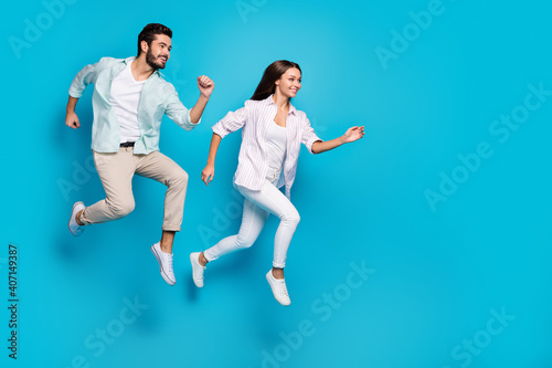 Photo of charming young couple wear casual shirt jumping running empty space isolated blue color background
