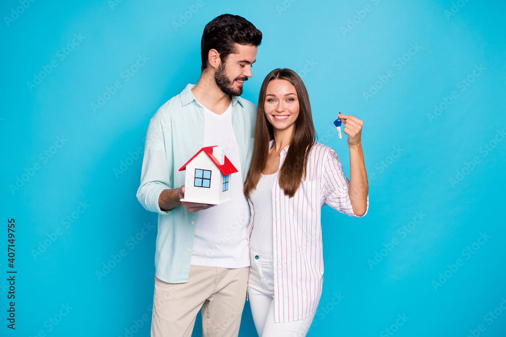 Photo of cute pretty young couple wear casual shirt holding small house keys isolated blue color background Photo of cute pretty young couple wear casual shirt holding small house keys isolated blue color background