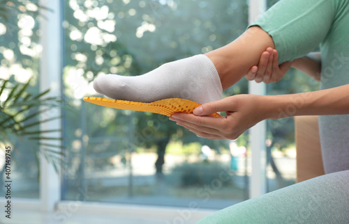 Woman fitting orthopedic insole indoors, closeup. Foot care