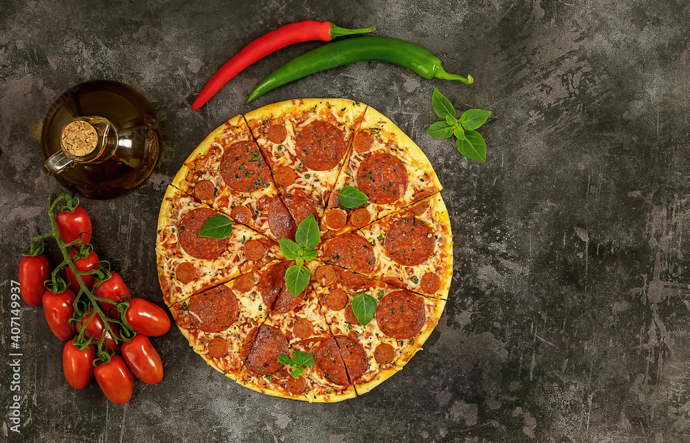 Tasty pepperoni pizza and cooking ingredients tomatoes, chili, basil on dark background.