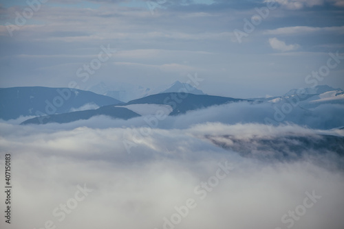 Awesome mountain landscape with sharp snowy mountain peak on horizon above clouds. Atmospheric minimal alpine scenery with pointed pinnacle above many low clouds. Cloudy sea  cloudy ocean in mountains