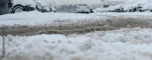 Fotografie Muddy splush on wet urban road with car track on parking lot