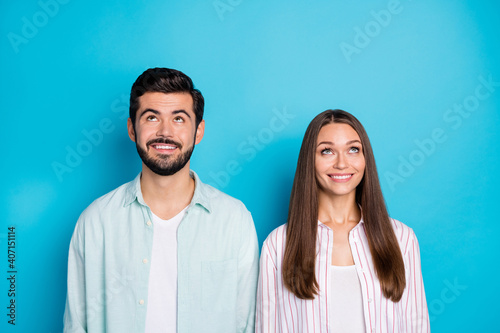 Photo of cheerful attractive spouses look empty space above good mood isolated on blue color background