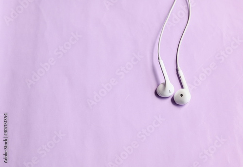 Top view of white earphones on light purple background, copy space
