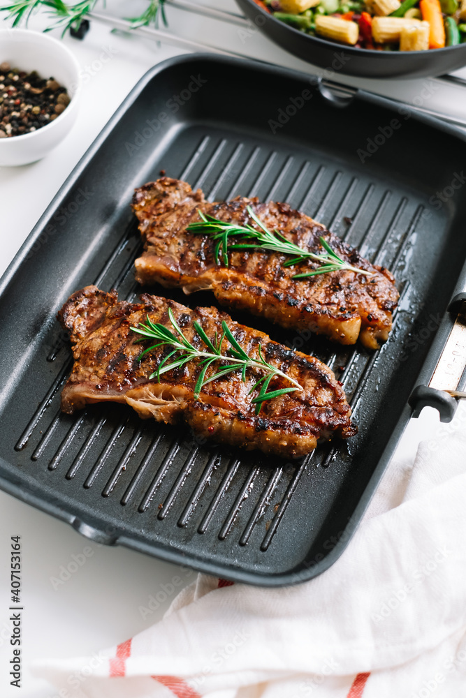 Grilled beef steak with rosemary in black grill pan on the table. Grilled beef steak with rosemary in black grill pan on the table.