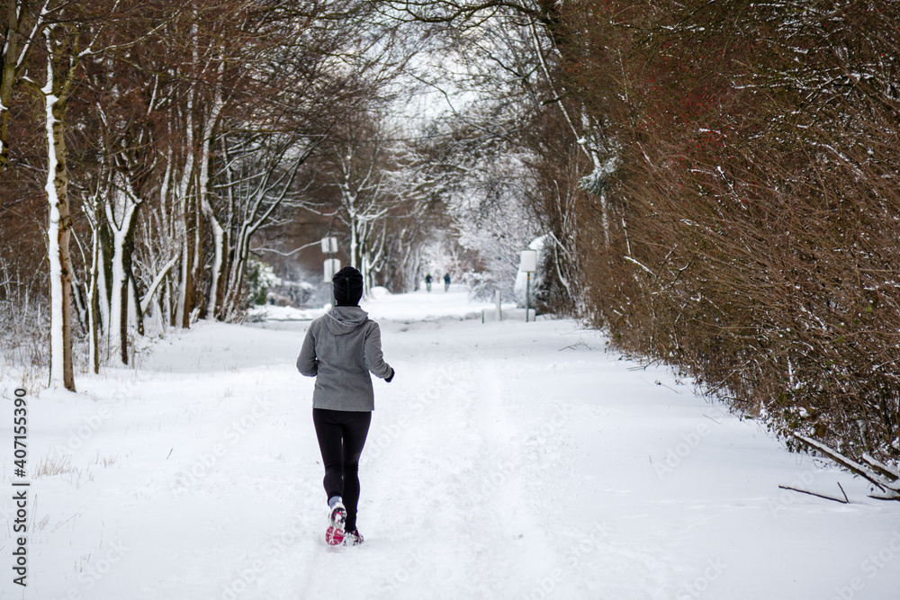 woman running in the snow between rows of trees