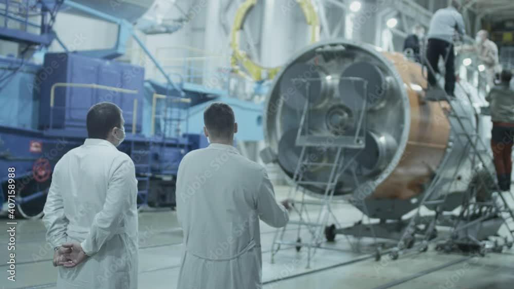 Two scientist engineers inspect the spacecraft, write on the tablet. A space rocket in a military hangar being prepared for launch. Space technologies. Construction of Big Rocket. Humanity in Space