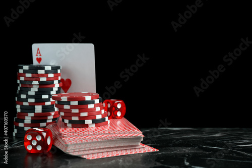 Gaming chips, dices and cards on dark marble table against black background