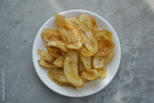 Deep fried banana chips mixed with sugar on a white plate. Center.